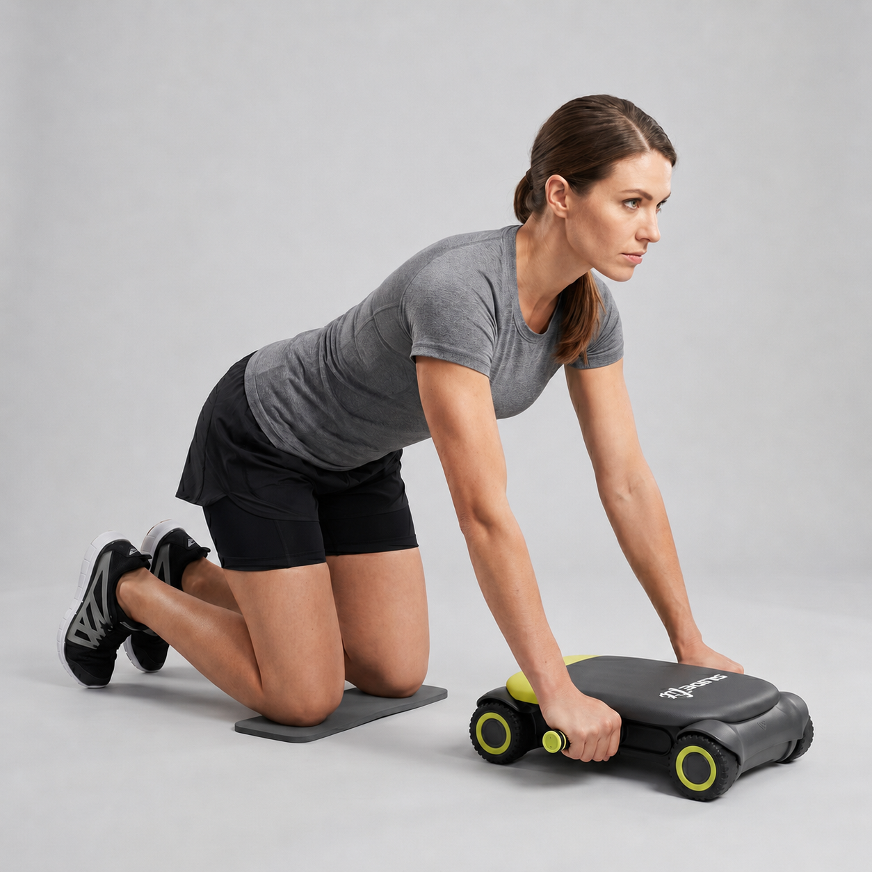 Woman in a gray tee and black shorts kneeling on a mat and rolling the Wonder Core Slide Fit four-wheel auto-rebound ab roller forward, demonstrating safe beginner kneeling form without straining the back