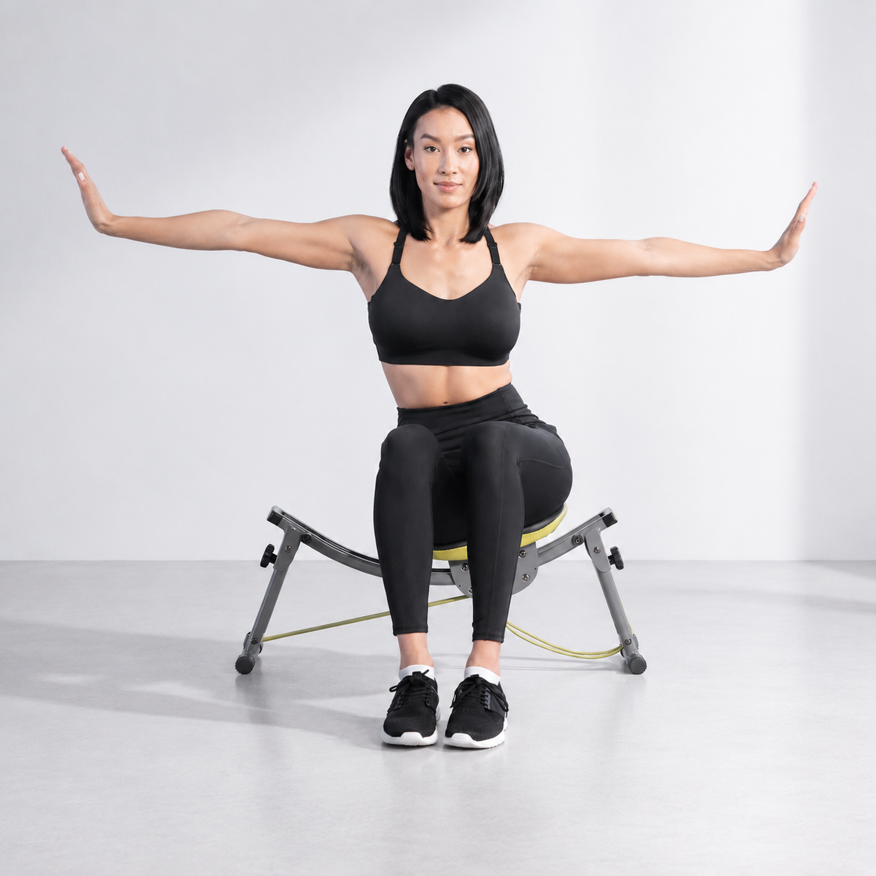 Woman in black activewear sitting on the Wonder Core Sway N Fit swing ab chair with arms extended to the sides for balance, demonstrating a low-impact seated core exercise for desk workers with lower back pain