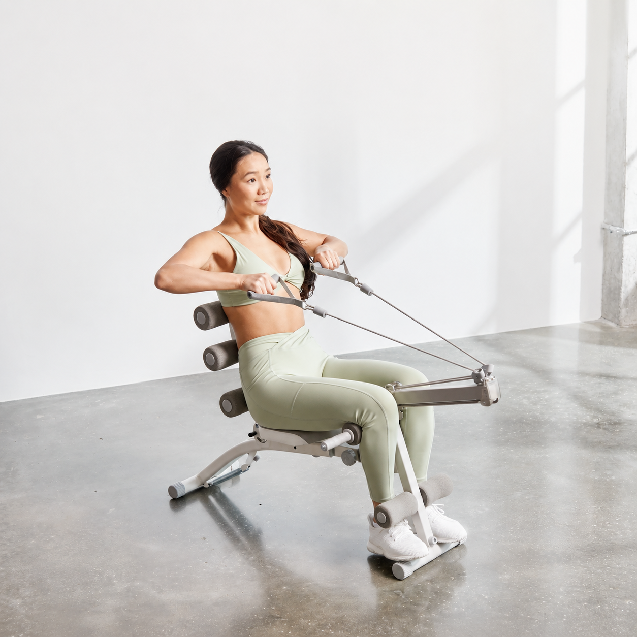 Woman using the Wonder Core 2 for seated rowing, pulling the 8-pulley resistance handles with her back against the foam rollers